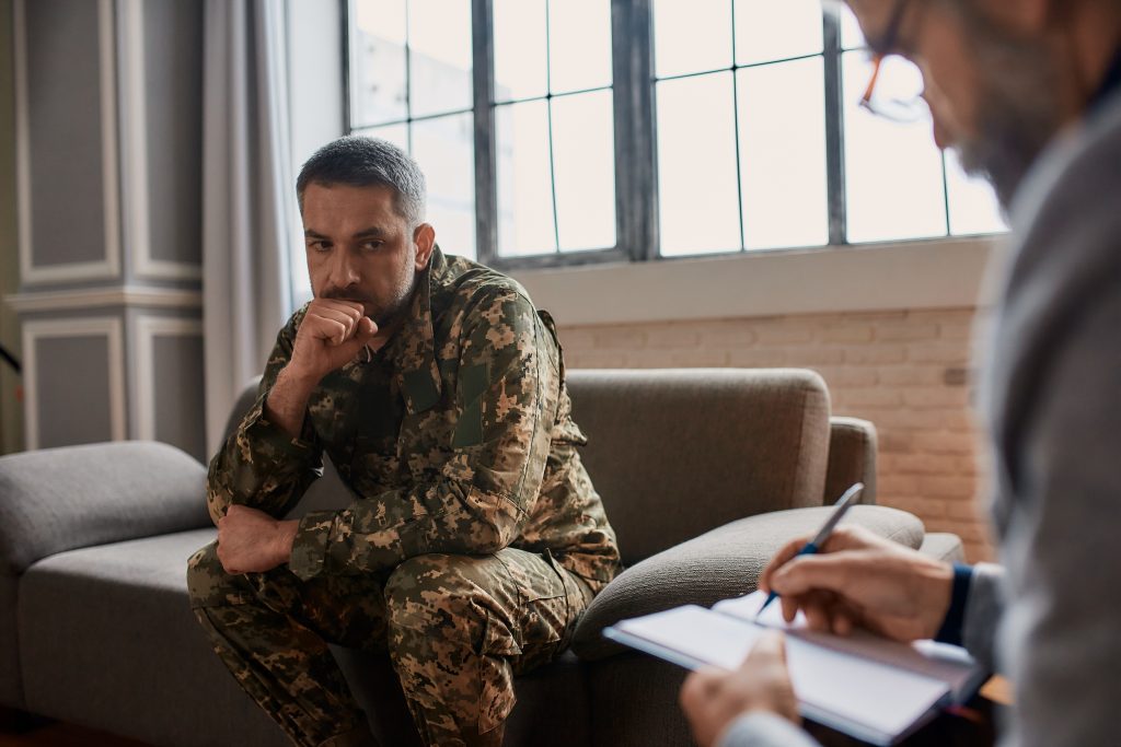 A veteran sitting on a couch, speaking with a therapist about CPTSD vs PTSD